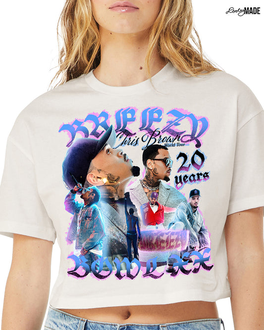 A model wearing A Vintage White crop top t-shirt with a pink, blue, and black graphic that says 'Breezy Bowl XX,' 'Chris Brown World Word Tour' and '20 Years.' The graphic also features a collection of stylized Chris Brown photos with pink and blue highlights.