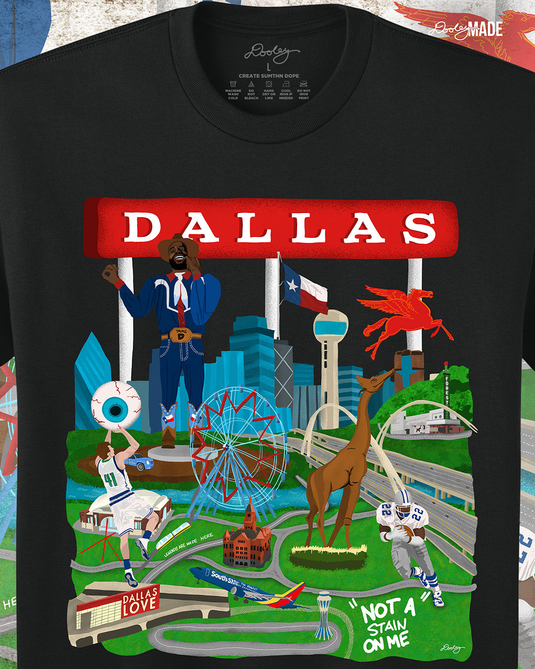 A black Dallas themed shirt with the text "Dallas" in red and illustrated Dallas landmarks like the Dallas skyline, Big Tex and the Texas Star Ferris Wheel at the State Fair of Texas, legendary Dallas athletes, Dallas Love Field Airport, Dallas Zoo giraffe statue, and the Margaret Hunt Hill Bridge. Shirt is zoomed to show detail.