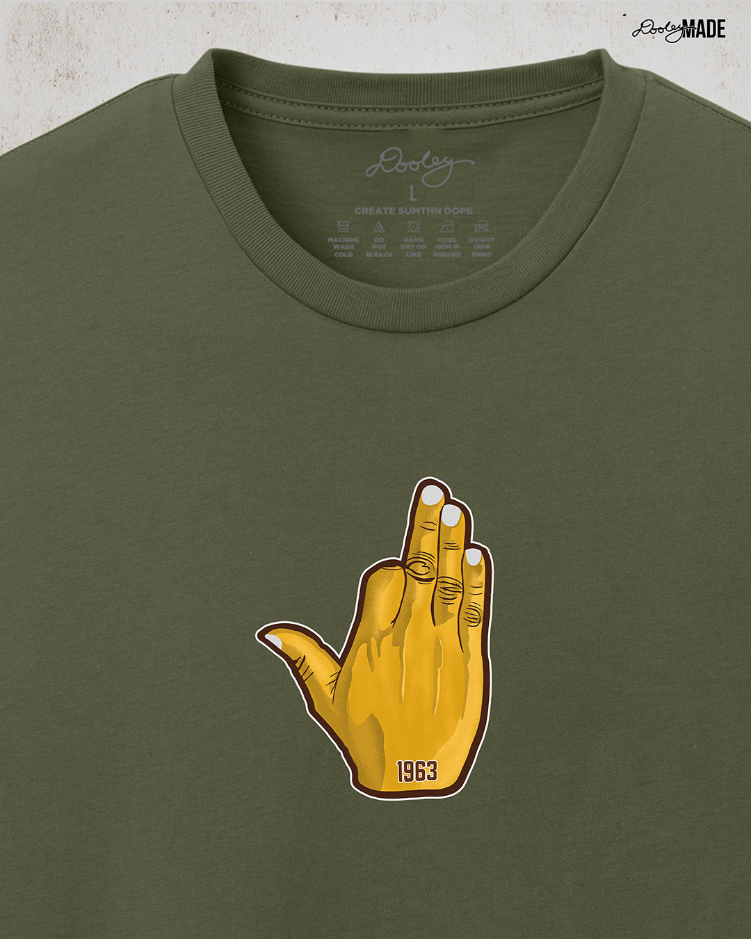 Image showing the front of a customizable Iota Phi Theta shirt with middle chest print of a gold, brown, and white "Ow-Ow" hand sign with "1963." Zoomed to show detail and placement. Shirt is on a textured white background.