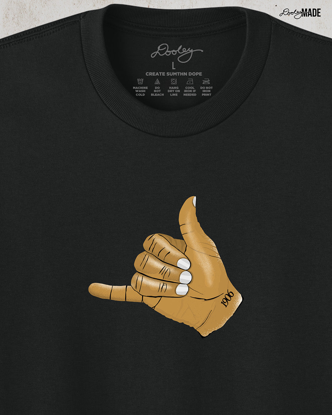 The front of a Black t-shirt with an old gold Alpha Phi Alpha Fraternity, Inc. "ICE" hand sign with "1906" text on the wrist. Image shows the design smaller on middle of the chest on the front. Image is cropped in to show detail.