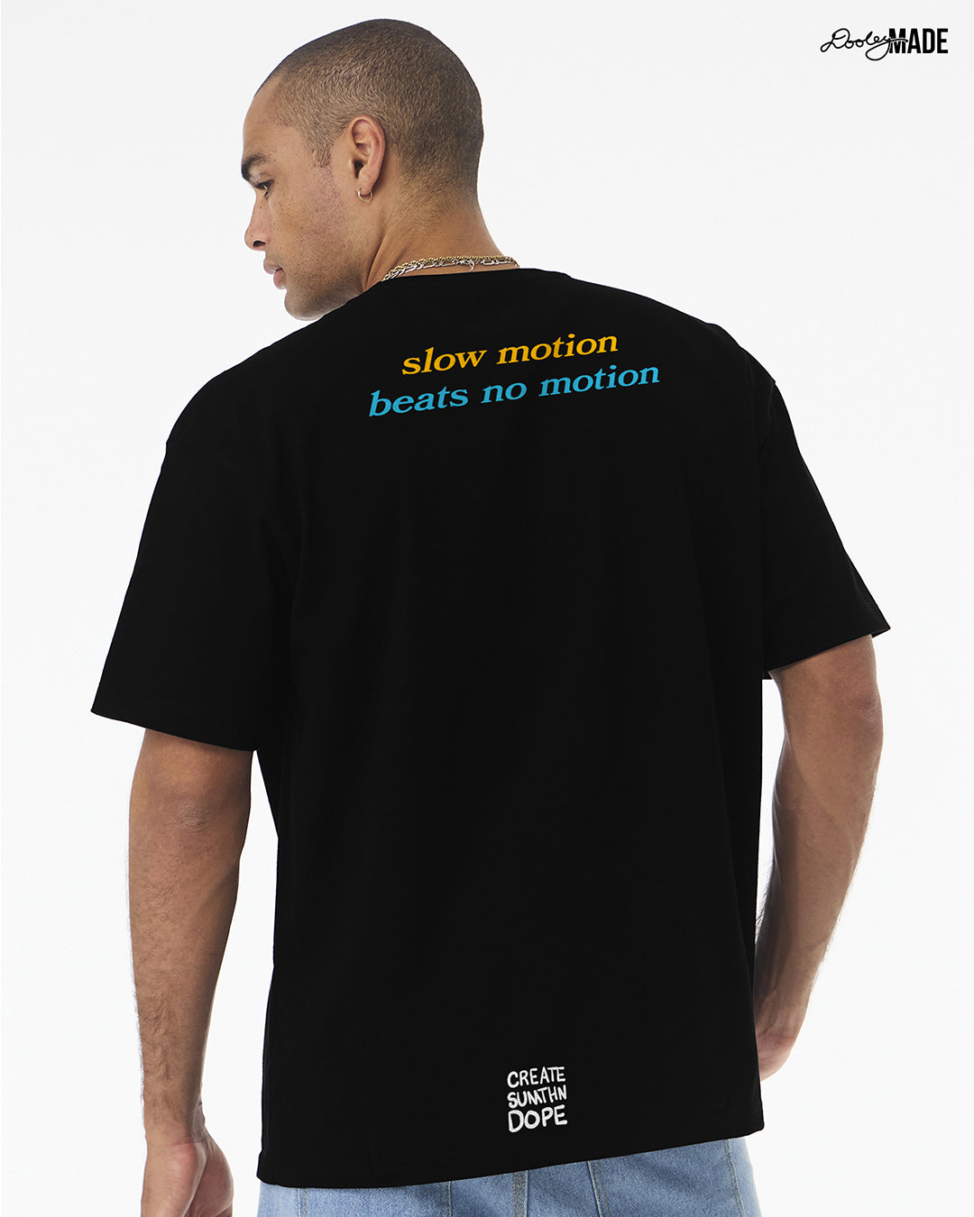 Person wearing a heavyweight black t-shirt with 'slow motion beats no motion' text on the back, standing against a white background.