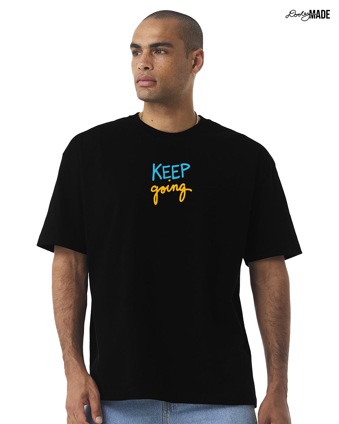 Man wearing a oversized heavyweight black t-shirt with 'KEEP going' text, standing against a white background.