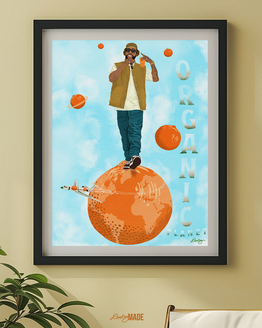 An image of a Larry June illustration inside of a black frame on a tan-yellow wall. The image shows him standing on an orange planet with floating orange planets, alongside the text "Organic Planet." There is also a orange themed jet flying from the right to left on the image.