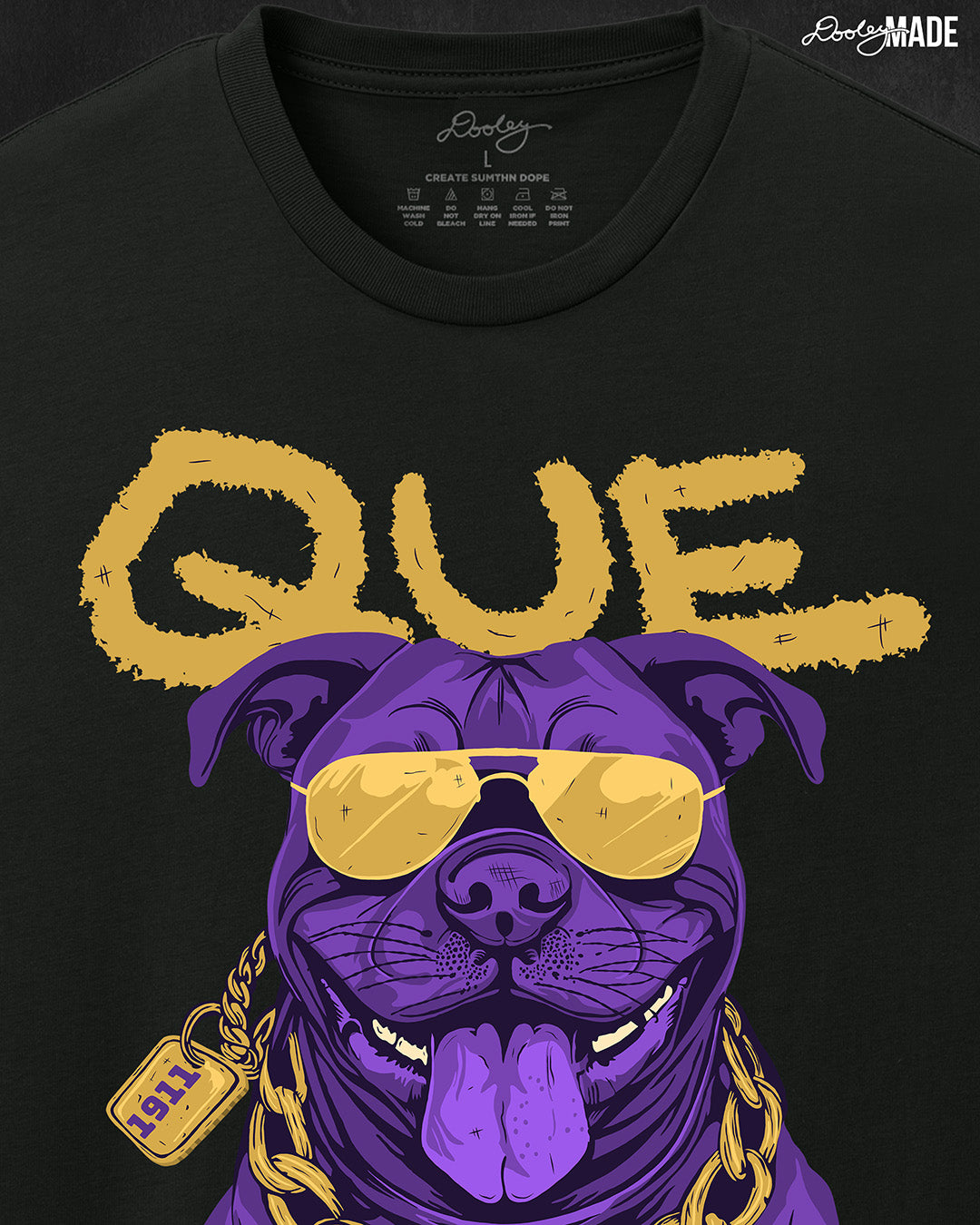 A zoomed in photo of the top of a white shirt with a graphic of an Omega Psi Phi Fraternity, Inc themed Pit Bull Dog wearing gold aviator sunglasses and a gold Omega Psi Phi necklace.