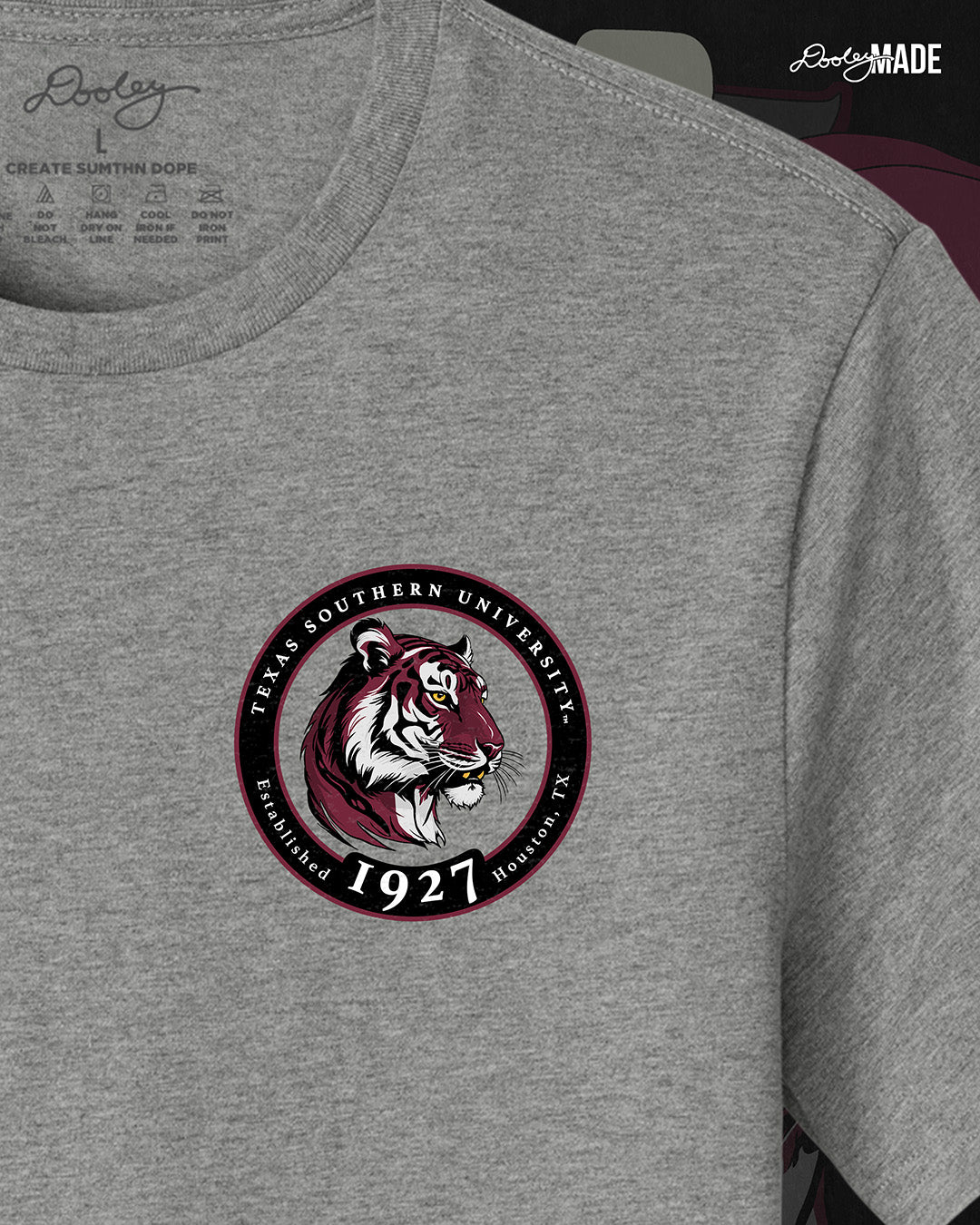 An image of the front of a heather gray Texas Southern University graphic tee shirt featuring a 3rd Ward University design and a maroon old school car with elbow rims. There is also a Scott St and Wheeler Ave street sign with a stop sign with the Texas Southern University logo on it.