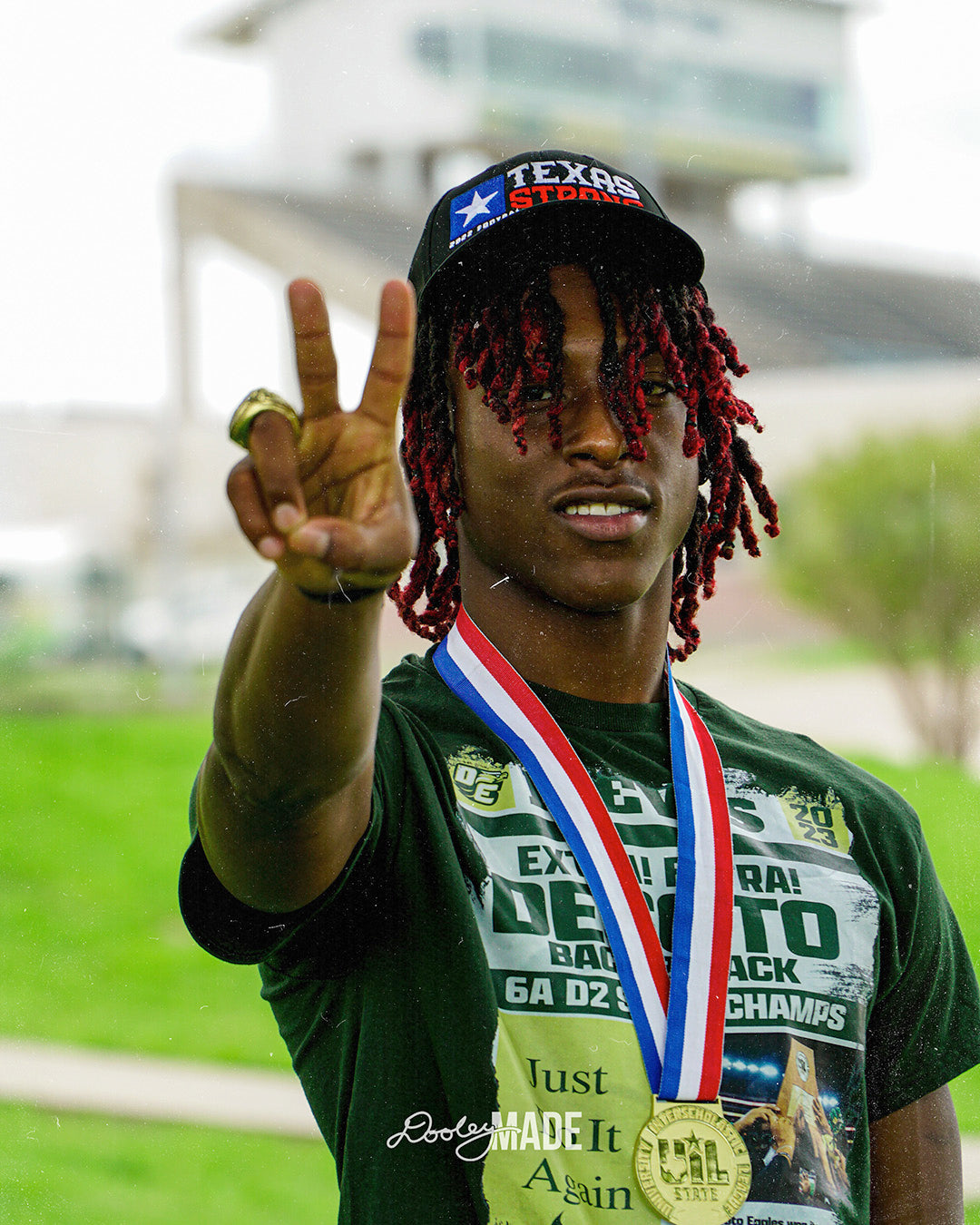 A photo advertising Personalized Graduation Photography showing a graduate holding up a peace sign white wearing a green shirt and a State UIL medal. The background features a towering football stadium. 