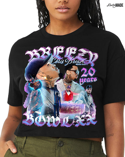 A model wearing a black crop top t-shirt with a pink, blue, and white graphic that says 'Breezy Bowl XX,' 'Chris Brown World Word Tour' and '20 Years.' The graphic also features a collection of stylized Chris Brown photos with pink and blue highlights. 