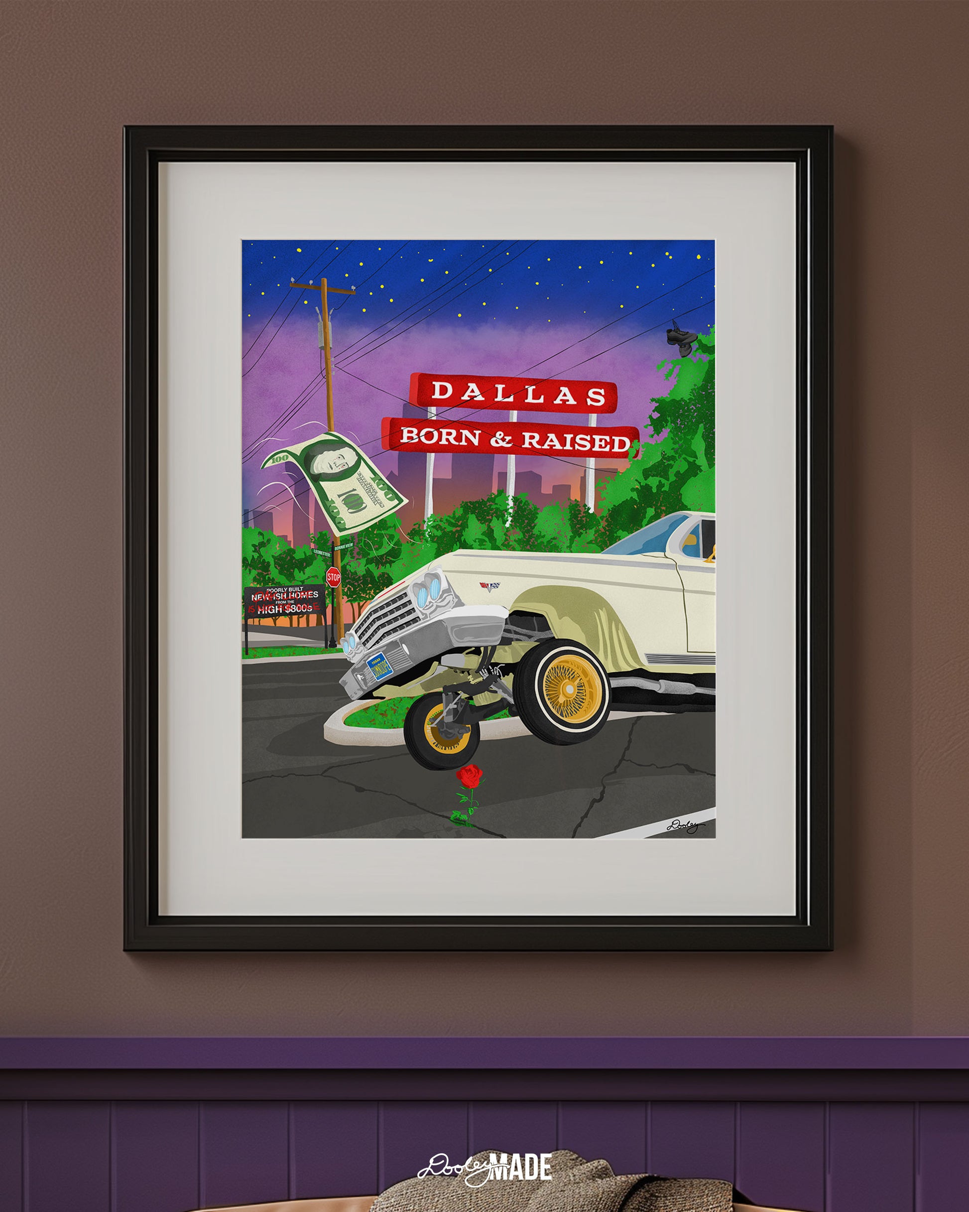 A frame on a wall holding a print of The Dallas Concrete Rose artwork - a vibrant illustration by Dre Dooley of a classic 1964 Chevy Impala lowrider with gold wire wheels, hopping in the streets of Dallas. A red street sign reads "Dallas Born & Raised", set against a sunset city skyline. A floating $100 bill, power lines, and urban elements reflect the culture of Dallas, TX. A single red rose grows from a cracked street, symbolizing resilience and roots.