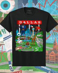The front of a Dallas themed shirt with the text "Dallas" in red and illustrated Dallas landmarks like the Dallas skyline, "Triple D Big Tex and the Texas Star Ferris Wheel at the State Fair of Texas, legendary Dallas athletes, Dallas Love Field Airport, Dallas Zoo giraffe statue, and the Margaret Hunt Hill Bridge. Background is colorful.