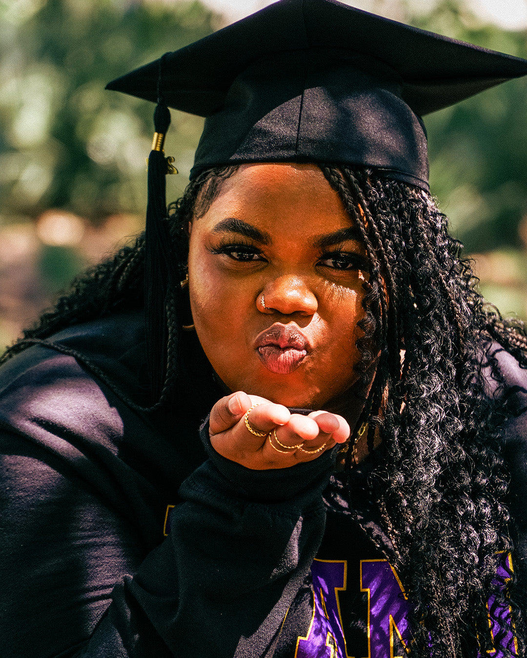 A warm photo advertising Personalized Graduation Photography showing a graduate wearing a graduation cap while blowing a kiss at the camera with a hand outstretched. 