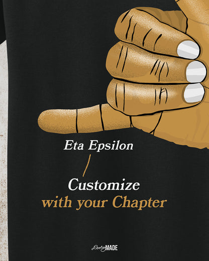 A customizable Black t-shirt with an old gold Alpha Phi Alpha Fraternity, Inc. "ICE" hand sign. The words "customize with your chapter" are listed to show customization option.