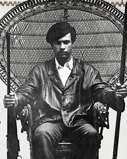 An zoomed image of Huey P. Newton artwork showing him sitting in a woven chair wearing a black leather jacket, dark colored pants, and a black cap while holding the barrel of a rifle in one hand and a wooden spear in the other.