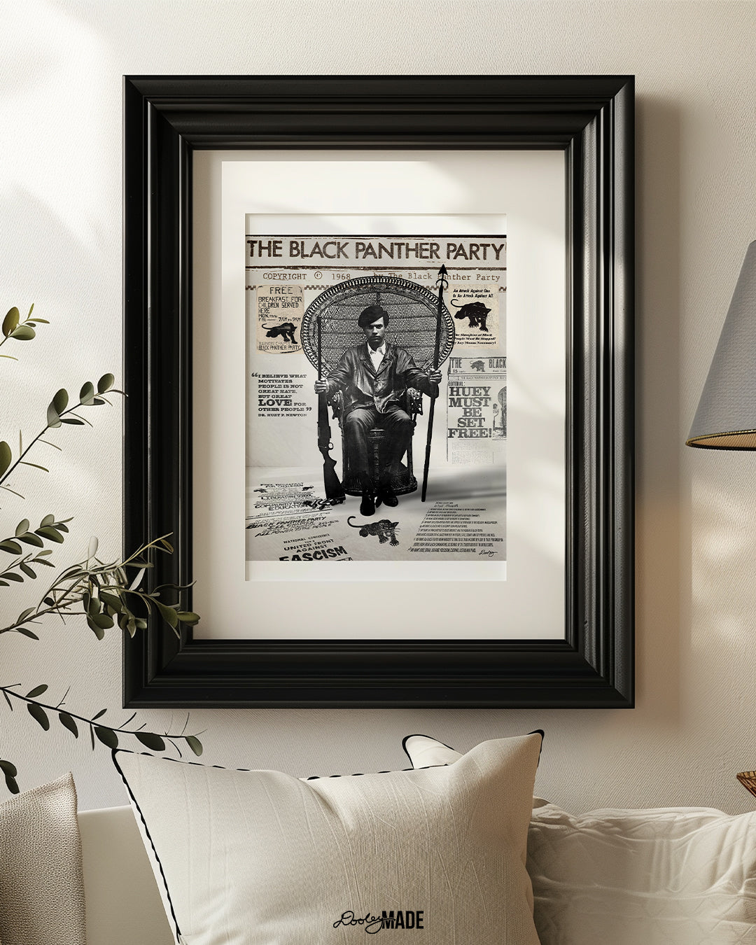 An image of framed Huey P. Newton artwork featuring the Black Panther Party's 10 Point Program, a poster that hung inside the door of the Chicago Chapter headquarters, the quote "I believe what motivates people is not great hate, but great love for other people," and other historical memorabilia. The frame is on the wall in a living room setting above  a cream colored couch.