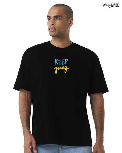 Man wearing a oversized heavyweight black t-shirt with 'KEEP going' text, standing against a white background.
