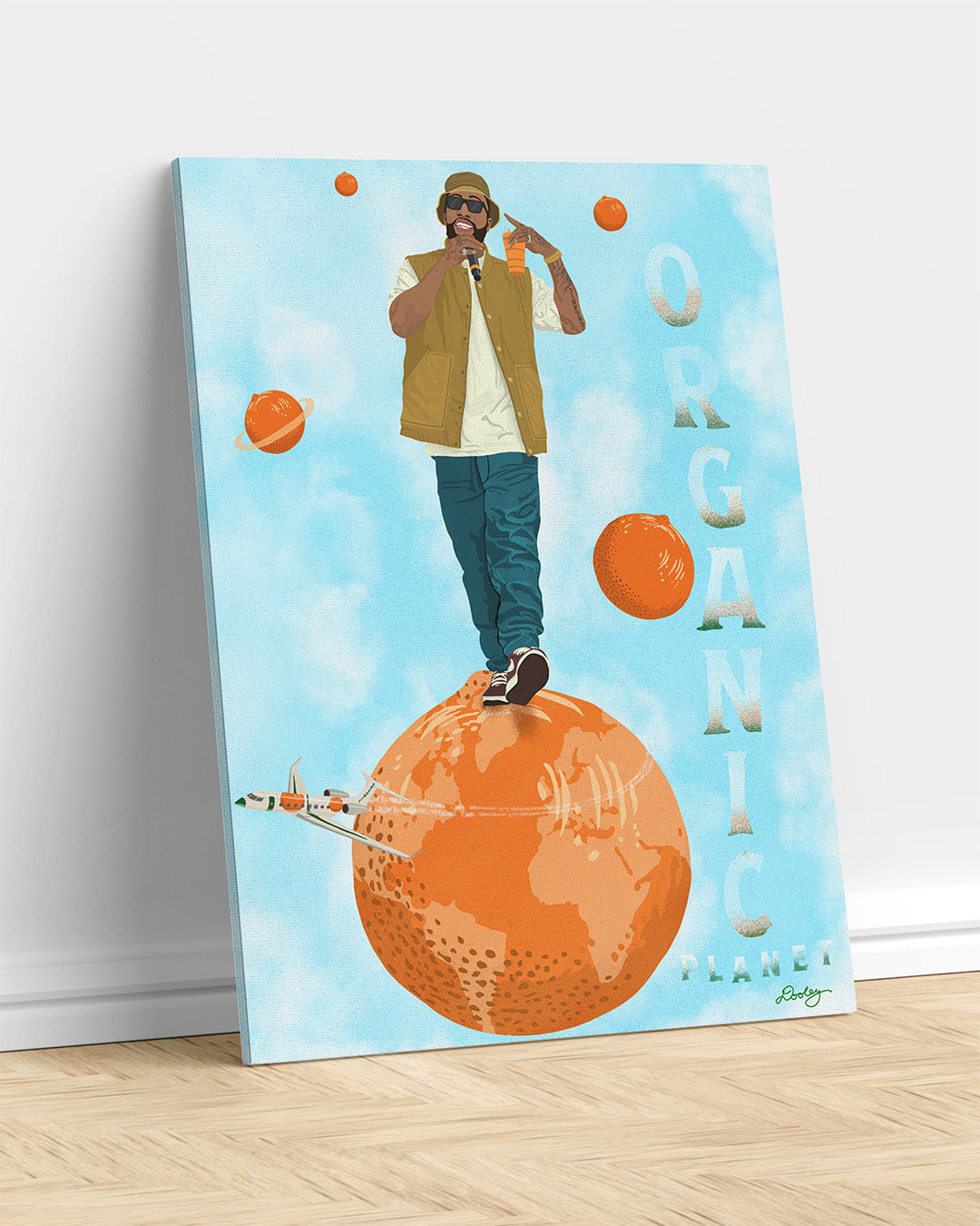 An image of a Larry June illustration on mounted canvas leaning against a white white wall. The image shows him standing on an orange planet with floating orange planets, alongside the text "Organic Planet." There is also a orange themed jet flying from the right to left on the image.