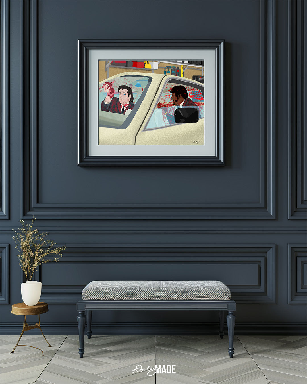 An image showing a framed photo of a stylized illustration by Dre Dooley titled "The Accident" depicting a scene from the movie Pulp Fiction on blue wall with small bench below.  Covered in blood, Samuel L. Jackson and John Travolta argue while cleaning blood and brain from a car's interior as it sits in a garage. 