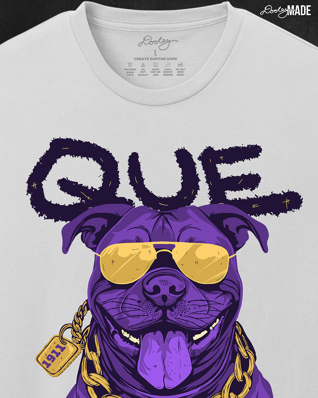 A zoomed in photo of the top of a white shirt with a graphic of an Omega Psi Phi Fraternity, Inc. themed Pit Bull Dog wearing gold aviator sunglasses and a gold Omega Psi Phi necklace.