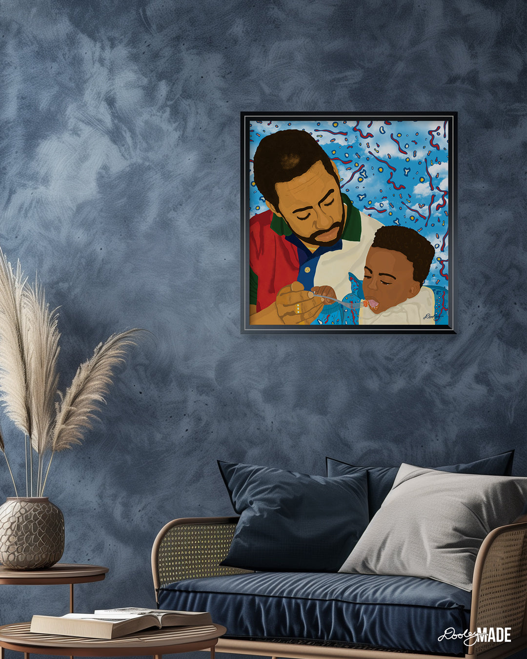 A soft, relaxing blue room with a chair, coffee table, and picture frame on a wall. The image in the frame is titled "Fatherhood In '91" is a vibrant illustration of a father lovingly feeding his young child. The father, in a red, green, and white shirt, and the child, in blue, are set against a dynamic background of blue sky with red, yellow, and white abstract shapes. This artwork captures the essence of Black fatherhood, conveying deep care and connection.