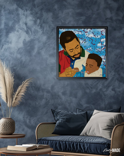 A soft, relaxing blue room with a chair, coffee table, and picture frame on a wall. The image in the frame is titled "Fatherhood In '91" is a vibrant illustration of a father lovingly feeding his young child. The father, in a red, green, and white shirt, and the child, in blue, are set against a dynamic background of blue sky with red, yellow, and white abstract shapes. This artwork captures the essence of Black fatherhood, conveying deep care and connection.