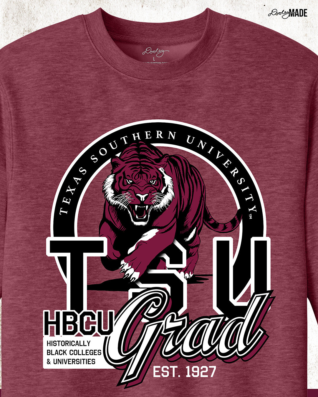 A heather maroon Texas Southern University graduation crewneck sweater featuring a prowling tiger surrounded by a circular frame with the university name inside of it, and the words "TSU Grad" next to HBCU and Historically Black Colleges & University, zoomed to show more detail.