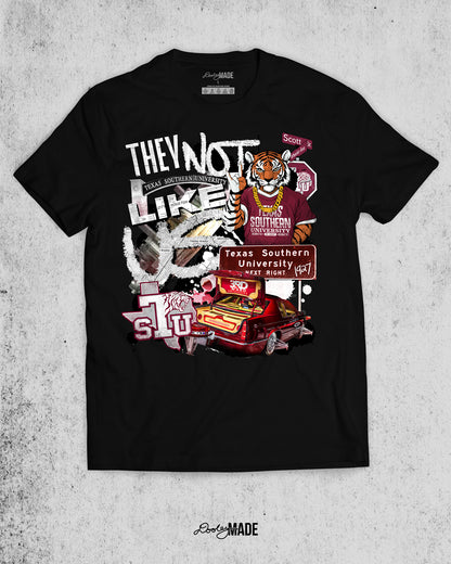 A "They Not Like Us" themed Texas Southern University black shirt featuring a vibrant collage with a hand drawn and graphic elements: a tiger wearing a gold chain, Scott St and Wheeler Ave street sign, the "Texas Southern University Next Right" interstate sign, a spilled Styrofoam cup, a textured TSU logo, and a maroon cadillac with swangers and adapters. 