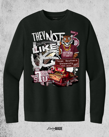A "They Not Like Us" themed Texas Southern University black crewneck sweater featuring a vibrant collage with a hand drawn and graphic elements: a tiger wearing a gold chain, Scott St and Wheeler Ave street sign, the "Texas Southern University Next Right" interstate sign, a spilled Styrofoam cup, a textured TSU logo, and a maroon cadillac with swangers and adapters. 