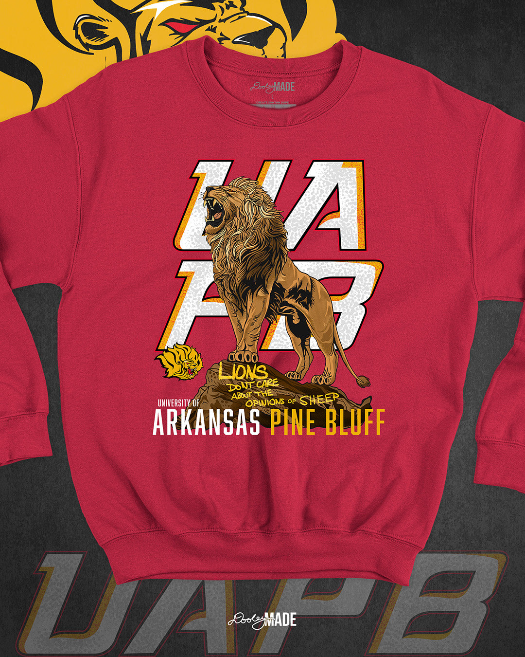The front of a red University of Arkansas Pine Bluff graphic crewneck sweater with the slogan "Lions Don't Care About The Opinions of Sheep" on the front with a Lion roaring on top of a rock in front of a stylized UAPB logo.