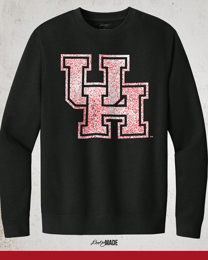 Image showing a black University of Houston crewneck sweatshirt with a white UH logo with red speckles stretched across the front.