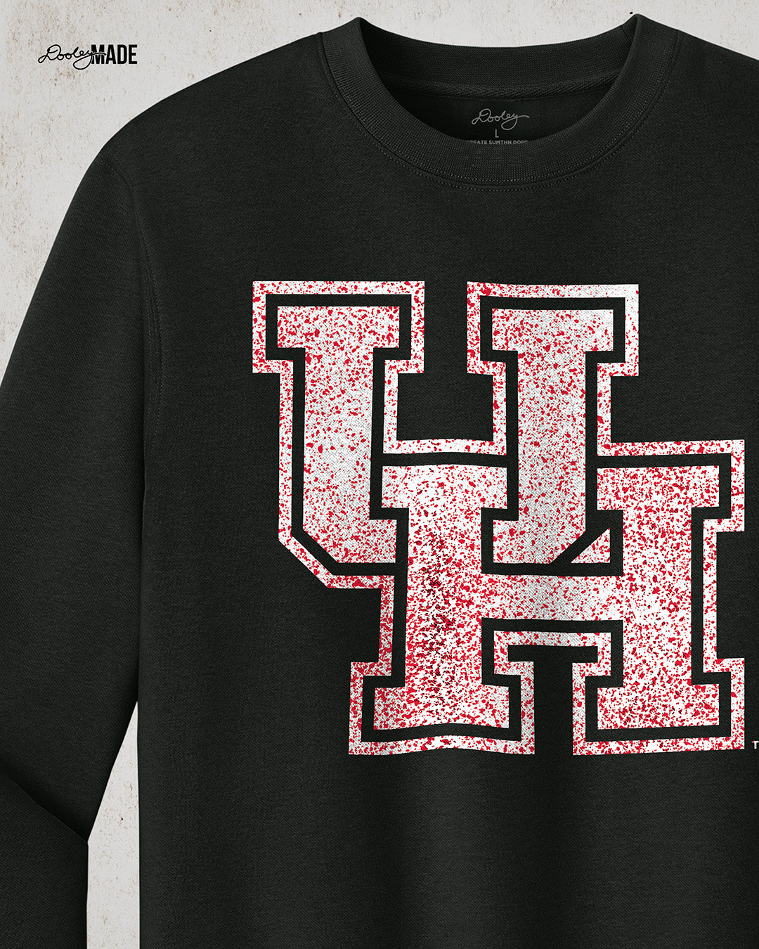 Image showing a black University of Houston crewneck sweatshirt with a white UH logo with red speckles stretched across the front, zoomed to show detail.
