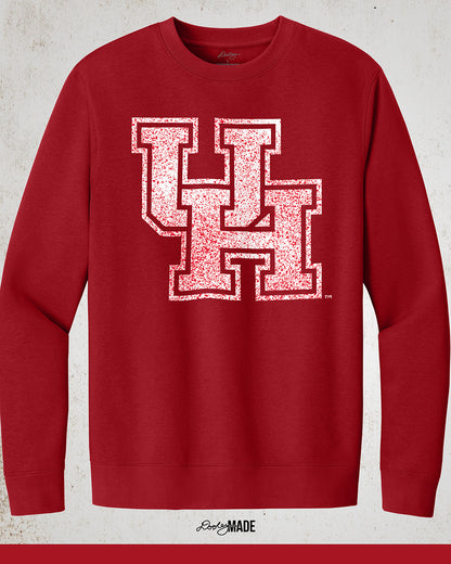 Image showing a red University of Houston crewneck sweatshirt with a white UH logo with red speckles stretched across the front.