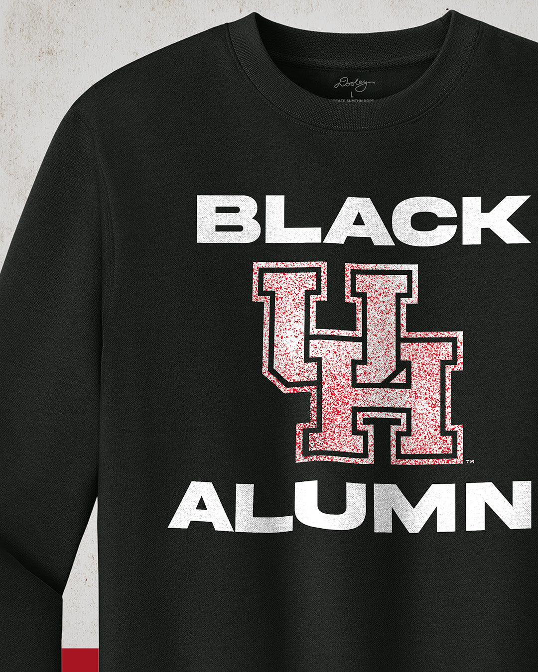 Image of a black University of Houston Black Alumni Crewneck Sweatshirt with bold, white text reading "BLACK ALUMNI" surrounding a speckled red "UH" logo in the center. The design highlights pride and unity for Black Alumni of the University of Houston, presented on a modern and stylish garment perfect for showing school spirit.
