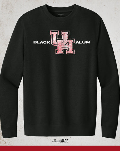 Image of a Black "Black UH Alumni crewneck sweater" showcasing bold, white text reading "BLACK ALUM" flanking a speckled white and red "UH" logo in the center. The design emphasizes pride and unity for Black alumni of the University of Houston, presented on a stylish and modern garment ideal for representing school spirit and Cougar pride.