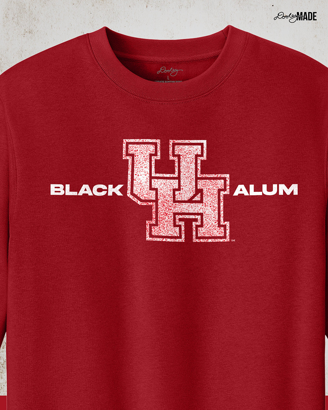 Image of a red "Black UH Alumni crewneck sweater" showcasing bold, white text reading "BLACK ALUM" flanking a speckled white and red "UH" logo in the center. The design emphasizes pride and unity for Black alumni of the University of Houston, presented on a stylish and modern garment ideal for representing school spirit and Cougar pride.
