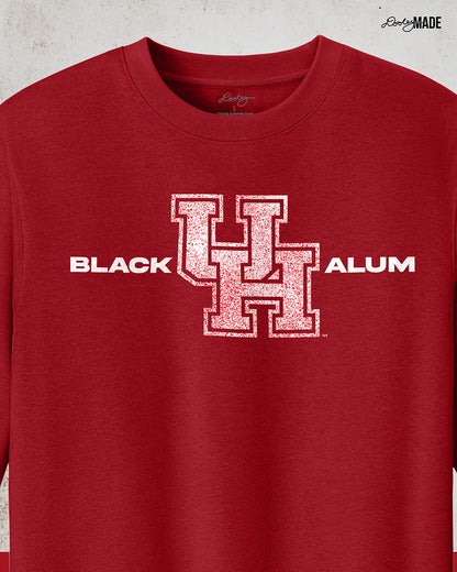 Image of a red "Black UH Alumni crewneck sweater" showcasing bold, white text reading "BLACK ALUM" flanking a speckled white and red "UH" logo in the center. The design emphasizes pride and unity for Black alumni of the University of Houston, presented on a stylish and modern garment ideal for representing school spirit and Cougar pride.