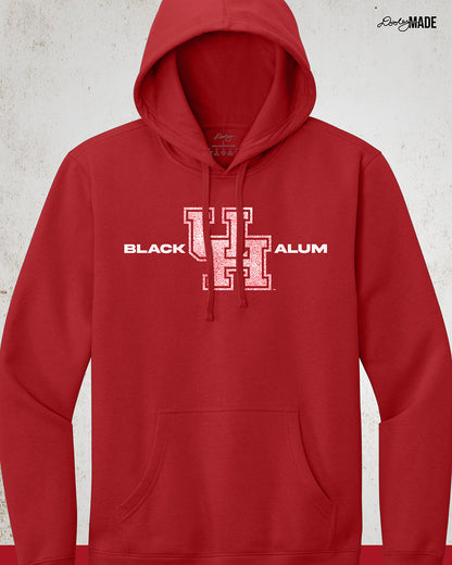 Image of a Black UH Alumni hoodie showcasing bold, white text reading "BLACK ALUM" flanking a speckled white and red "UH" logo in the center. The design emphasizes pride and unity for Black alumni of the University of Houston, presented on a stylish and modern garment ideal for representing school spirit and Cougar pride.