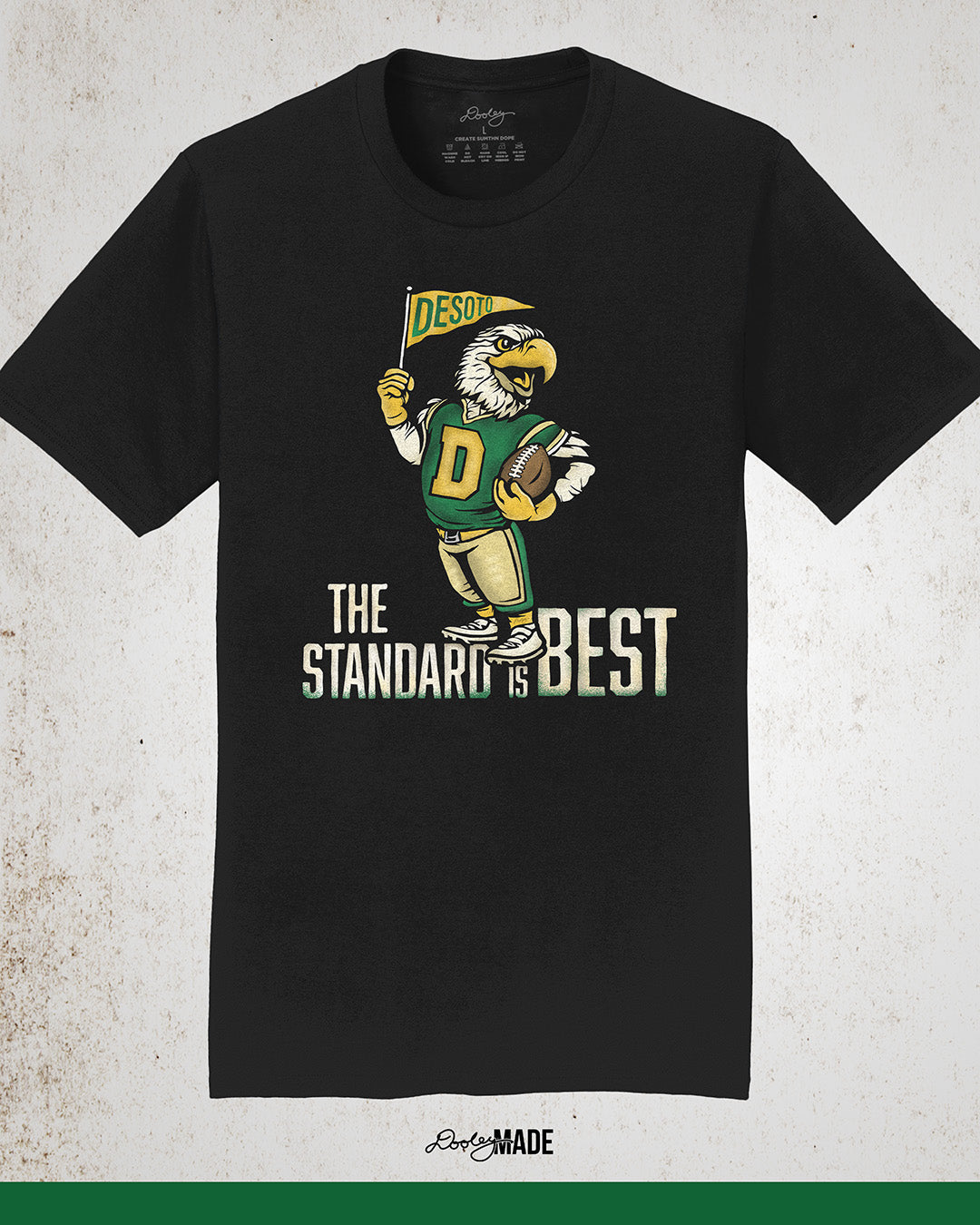 Vintage black shirt featuring a retro-inspired eagle mascot holding a football and waving a "DeSoto" Pennant flag. Bold text reads "The Standard is Best," accented with green and gold colors, celebrating DeSoto High School pride and tradition.