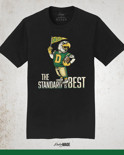 Vintage black shirt featuring a retro-inspired eagle mascot holding a football and waving a "DeSoto" Pennant flag. Bold text reads "The Standard is Best," accented with green and gold colors, celebrating DeSoto High School pride and tradition.