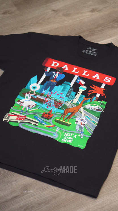 A video advertising a black Dallas themed shirt with the text "Dallas" in red and illustrated Dallas landmarks like the Dallas skyline, Big Tex and the Texas Star Ferris Wheel at the State Fair of Texas, legendary Dallas athletes, Dallas Love Field Airport, Dallas Zoo giraffe statue, and the Margaret Hunt Hill Bridge. Shirt is zoomed to show detail.